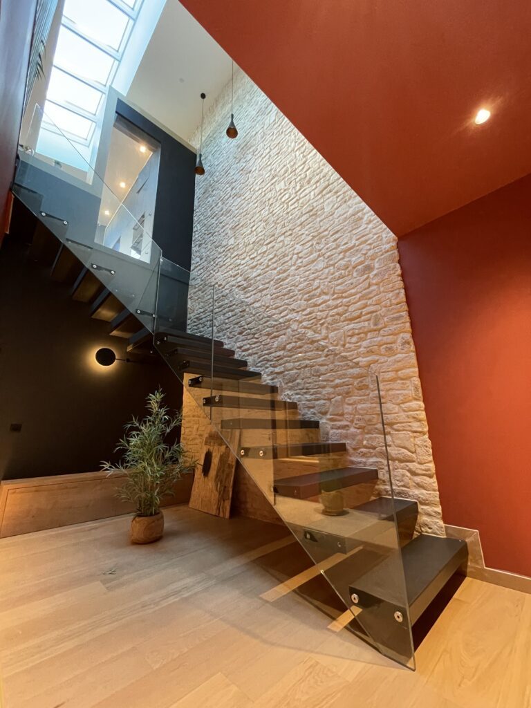 Escalier suspendu sous verrière, mur de pierre et murs rouges