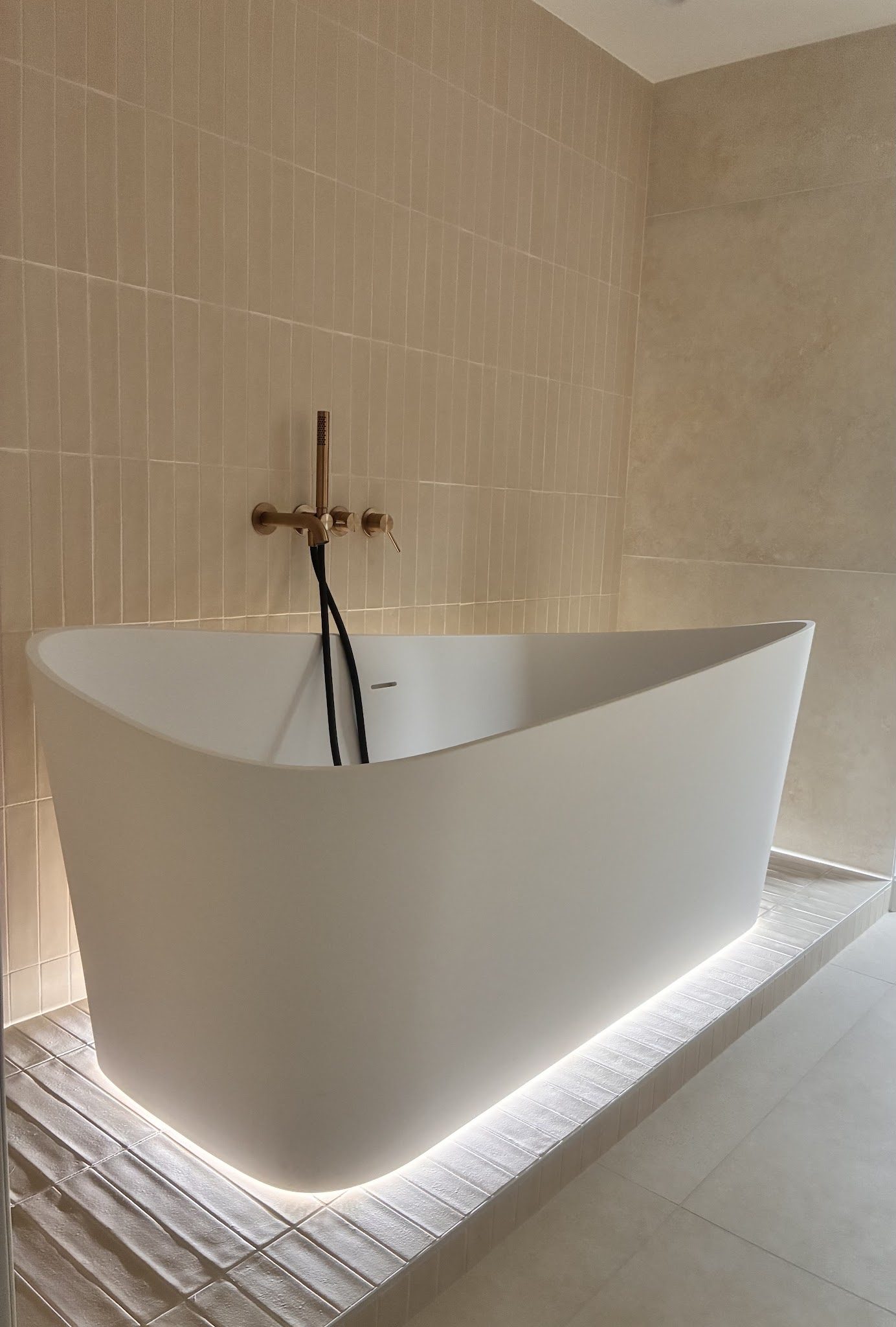 Baignoire îlot sur socle carrelé, baguettes beige au mur